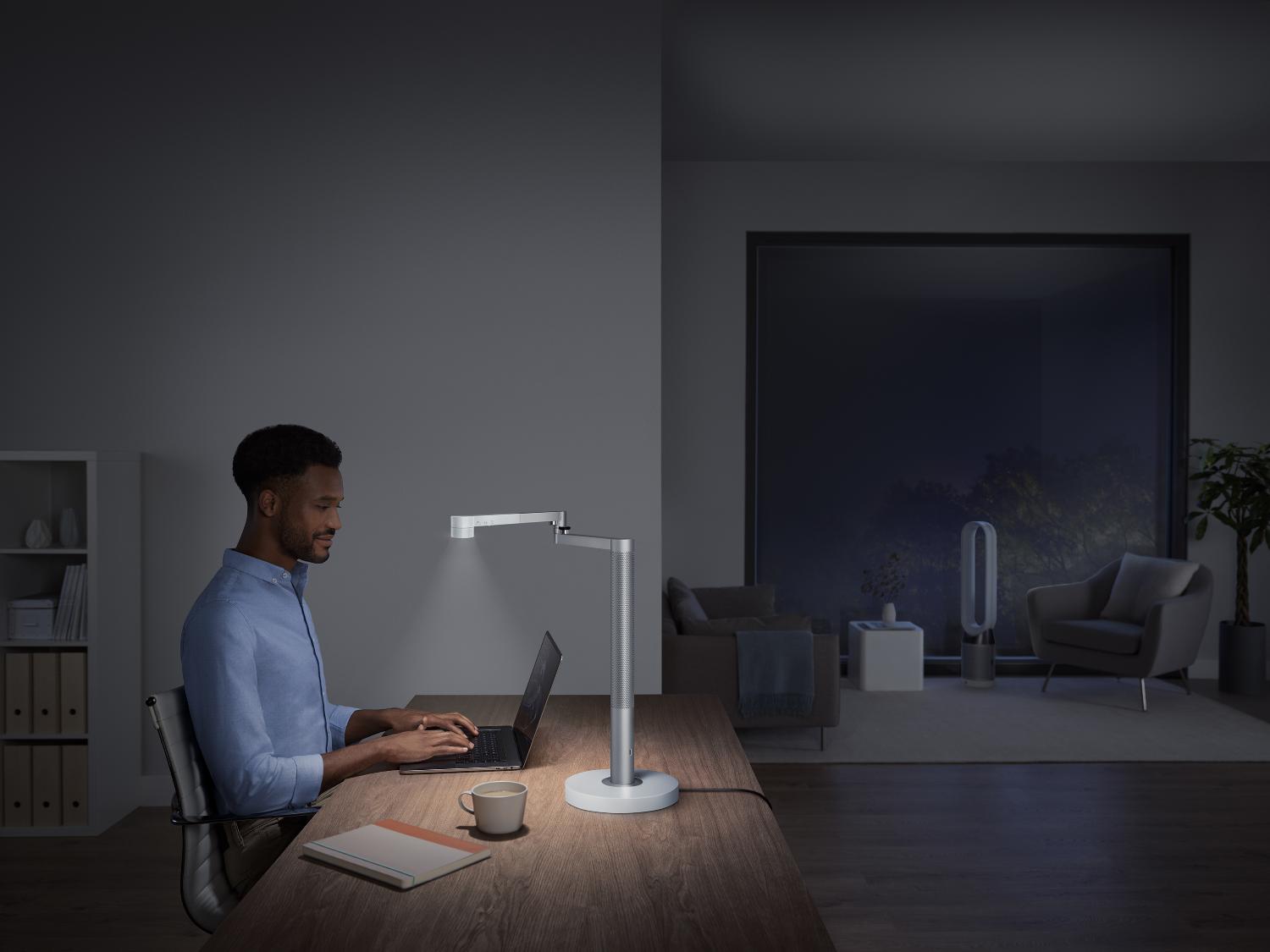 Man werkt achter bureau, gebruikmakend van de Dyson Solarcycle Morph lamp